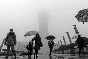 13日,行人冒雨走在霧霾籠罩下的杭州市區(qū)的一個廣場附近。新華社發(fā)